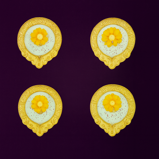 Amber Bloom Diya Candle Set by Karigar Kutir — set of four handcrafted soy wax fragrant candles in golden holders with yellow marigold floral designs, displayed on a deep plum background for Diwali gifting and festive décor.