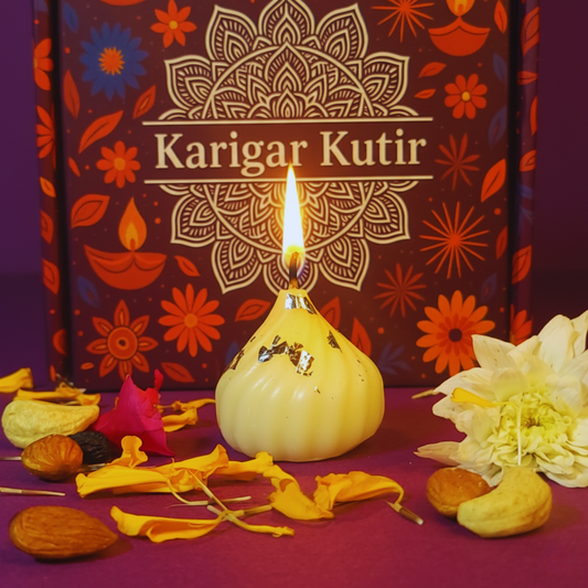 Lit Modak-shaped soy wax candle with silver varq detailing, placed before a Karigar Kutir maroon festive box, surrounded by marigold petals, nuts, and white flowers — symbolizing handmade luxury and Diwali warmth.
