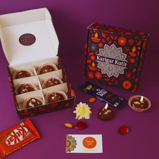 Karigar Kutir festive gift box featuring handmade Gulab Jamun-shaped candles with silver varq detailing, paired with chocolates, a thank-you card, and decorative petals — captured in warm festive lighting for Diwali gifting.